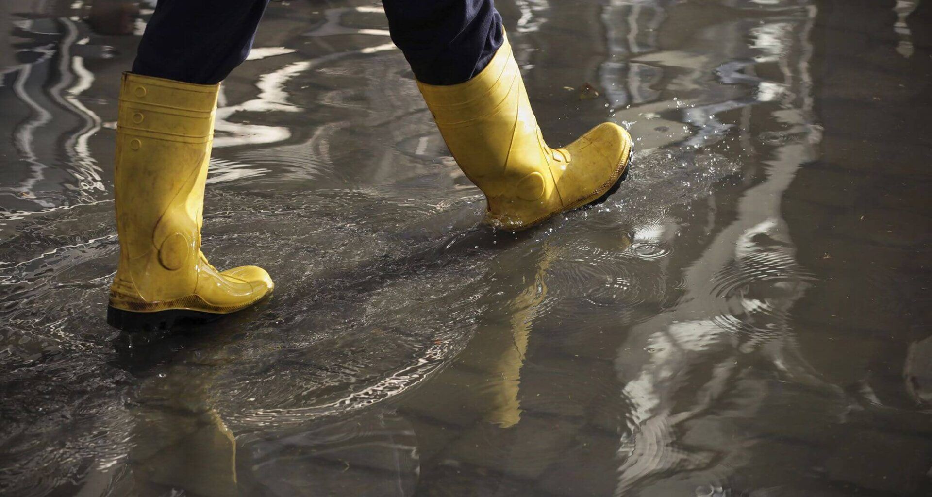 seguro cobre enchente: bota de plástico andando em ambiente alagado