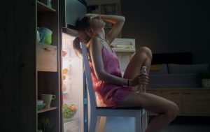 Woman Suffering From The Heat And Sitting In Front Of The Open Fridge